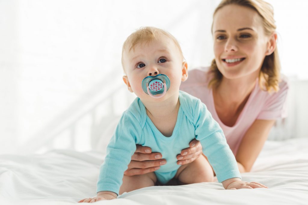 Smiling mother holding infant daughter with baby dummy